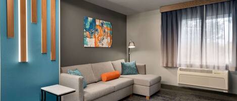 A modern living room with a sectional sofa, a small side table, a painting on the wall, and a large window with curtains.