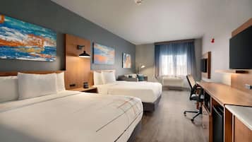 Habitación de hotel con dos camas, un escritorio con computadora, televisor y obras de arte en las paredes.