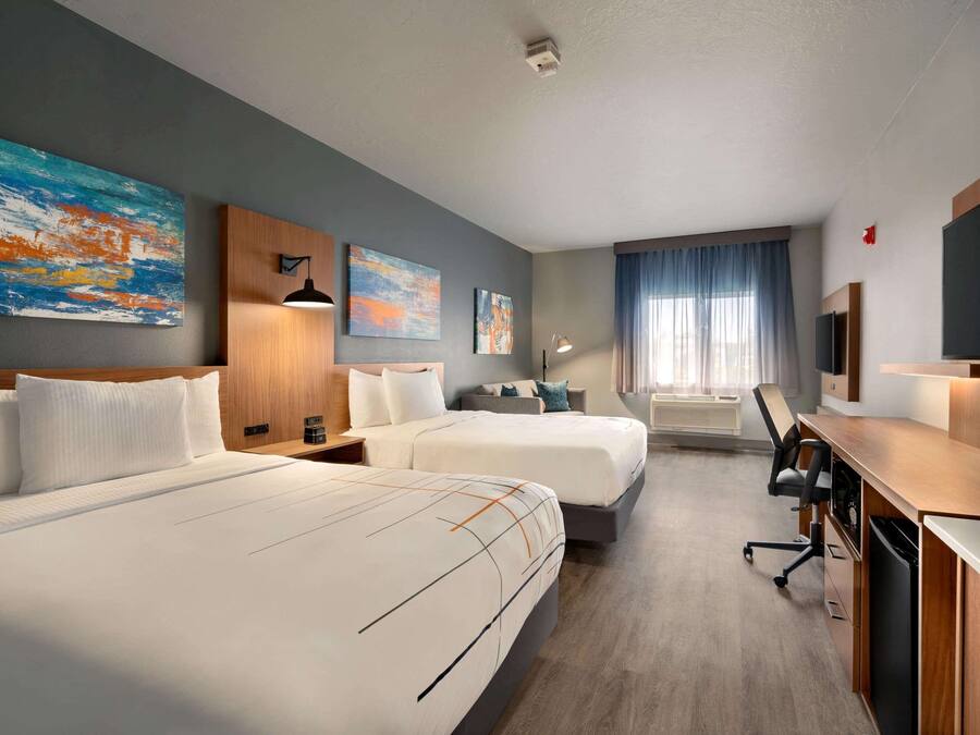 Habitación de hotel con dos camas, un escritorio con computadora, televisor y obras de arte en las paredes.