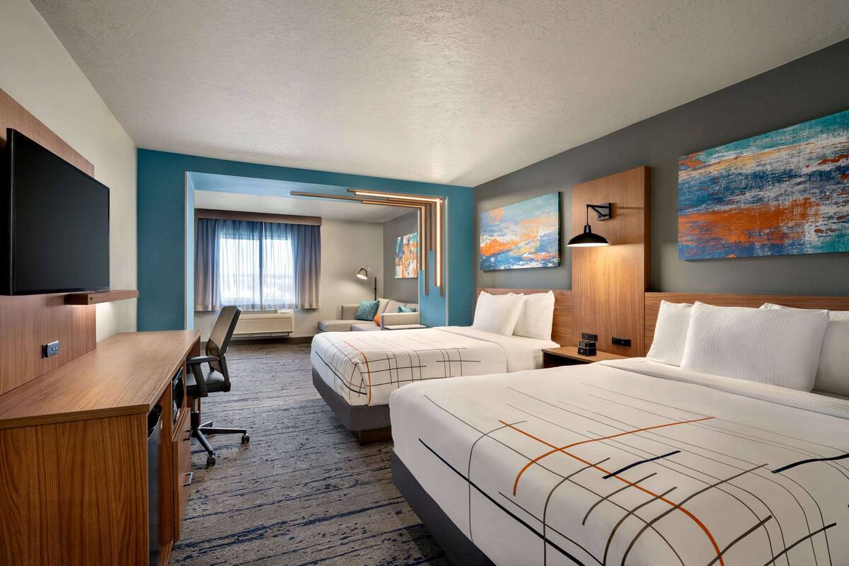 A hotel room with two beds, a desk, a chair, a TV, and artwork on the walls.