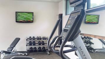 A gym with a treadmill, weight racks, and two TVs displaying sports games.