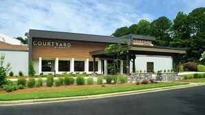 Ein Hotel der Courtyard by Marriott mit modernem Design, das eine überdachte Terrasse und eine angelegte Grünfläche bietet.