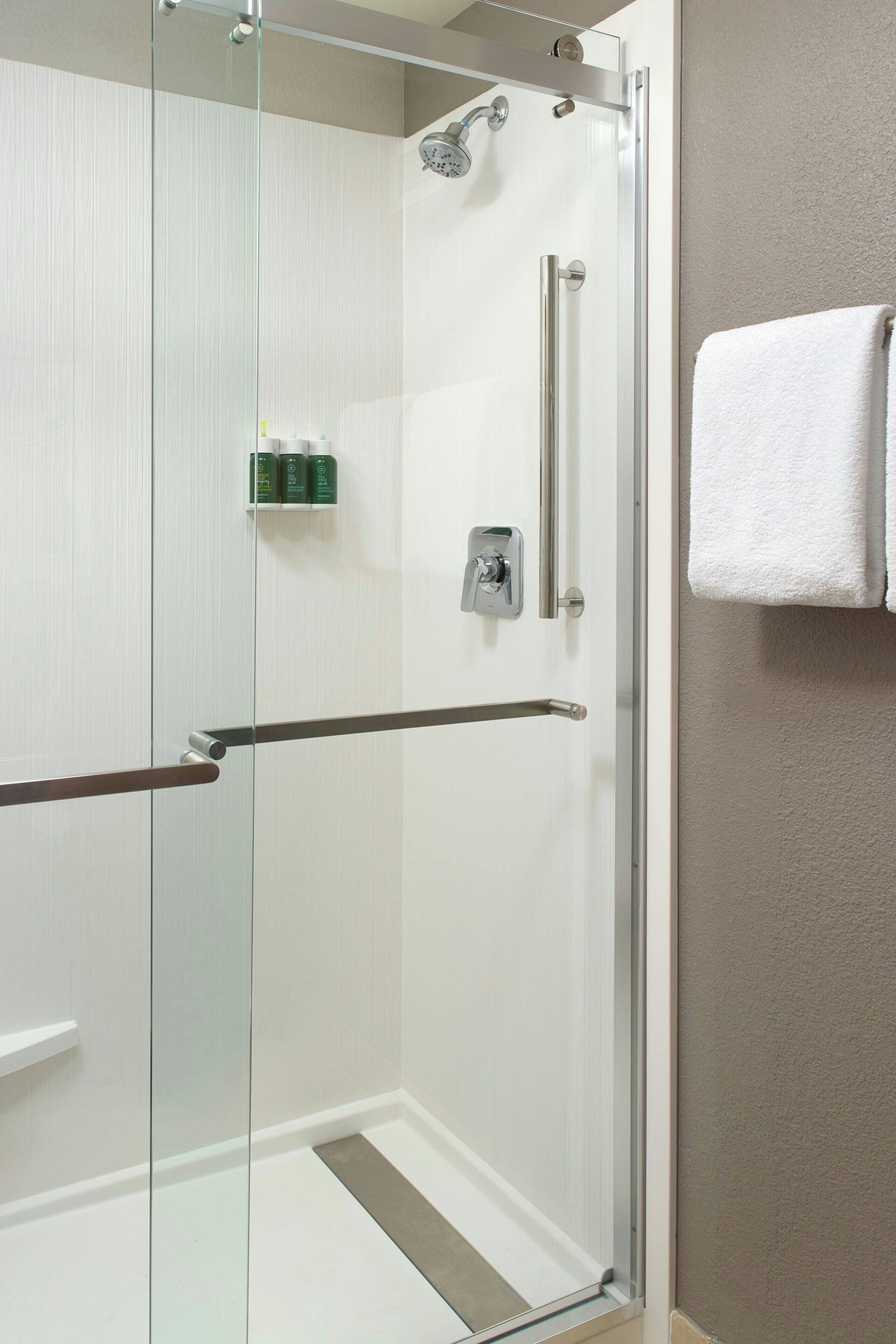 A glass-enclosed shower with a handrail, a towel rack, and a small shelf with toiletries.