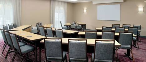 A conference room with multiple tables and chairs, a projector screen, and a carpeted floor.
