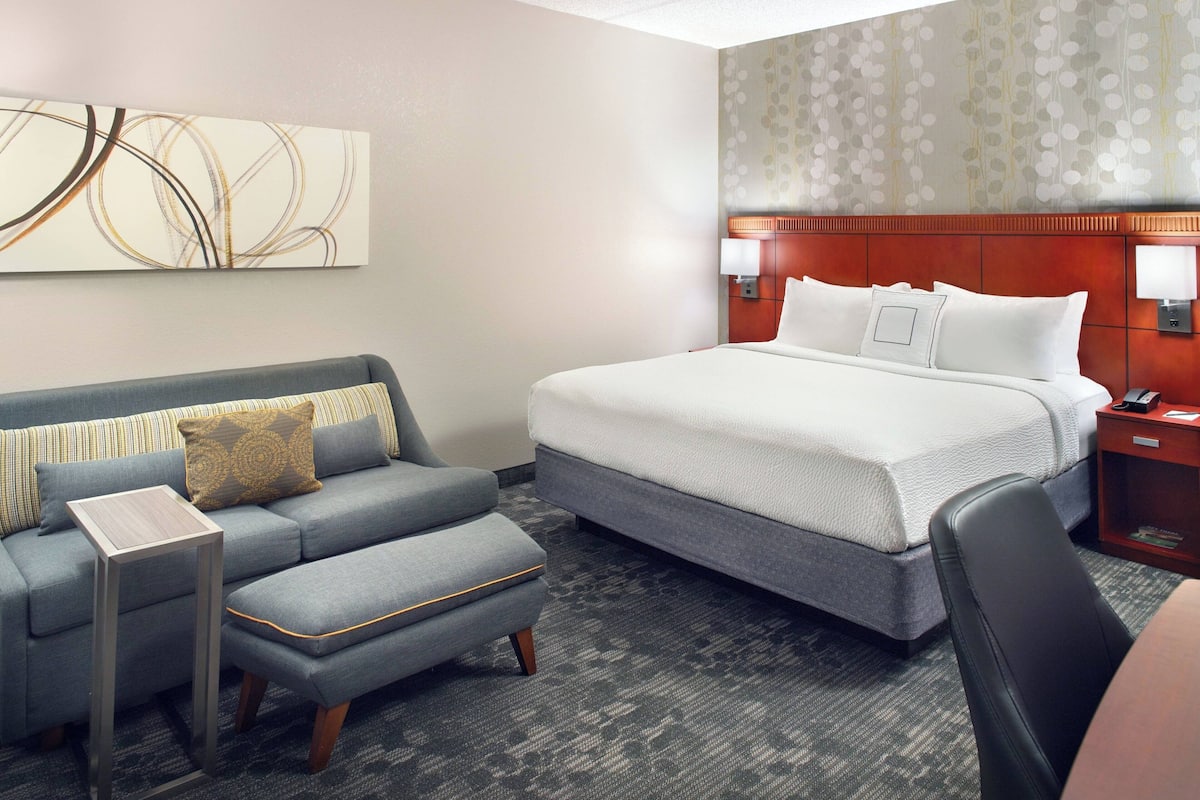 A hotel room with a bed, a sofa, a small table, and a nightstand.