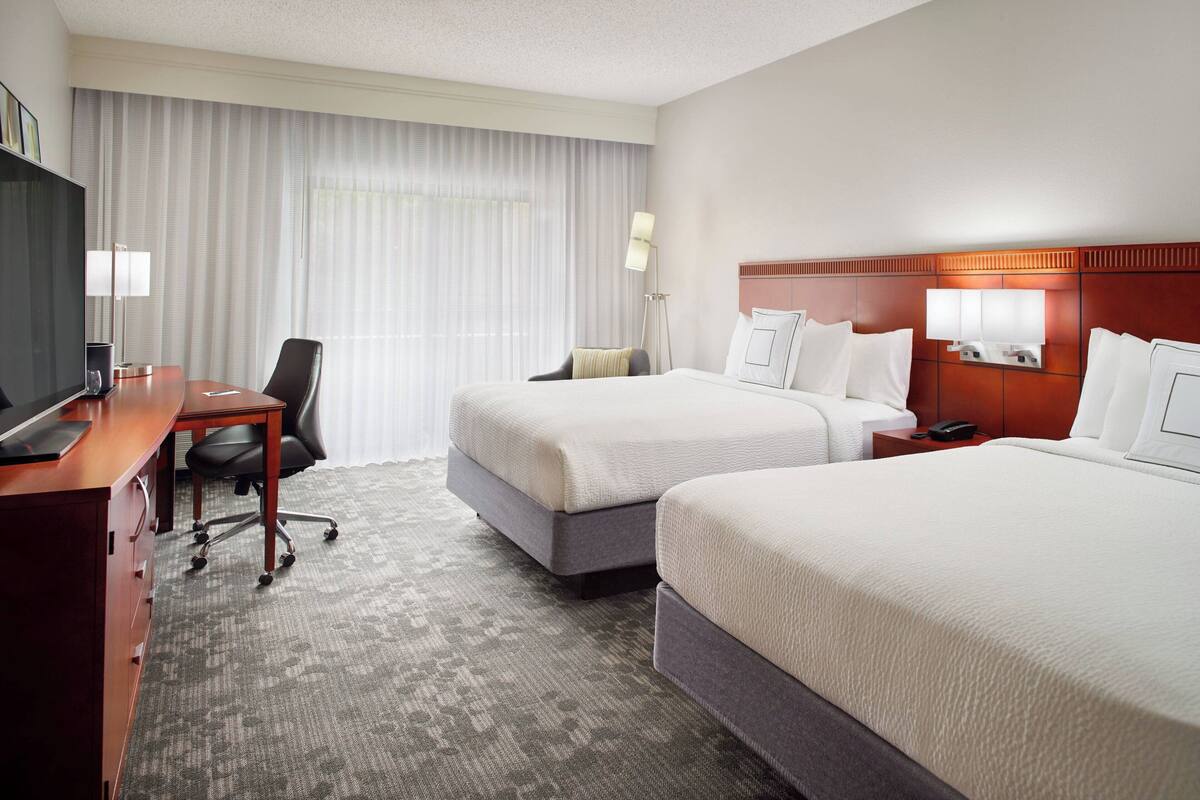 A hotel room with two beds, a desk, a chair, and a television.