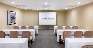 Ein Konferenzraum im Indian Wells Resort Hotel mit mehreren Tischen, Stühlen und einer Projektionsleinwand.