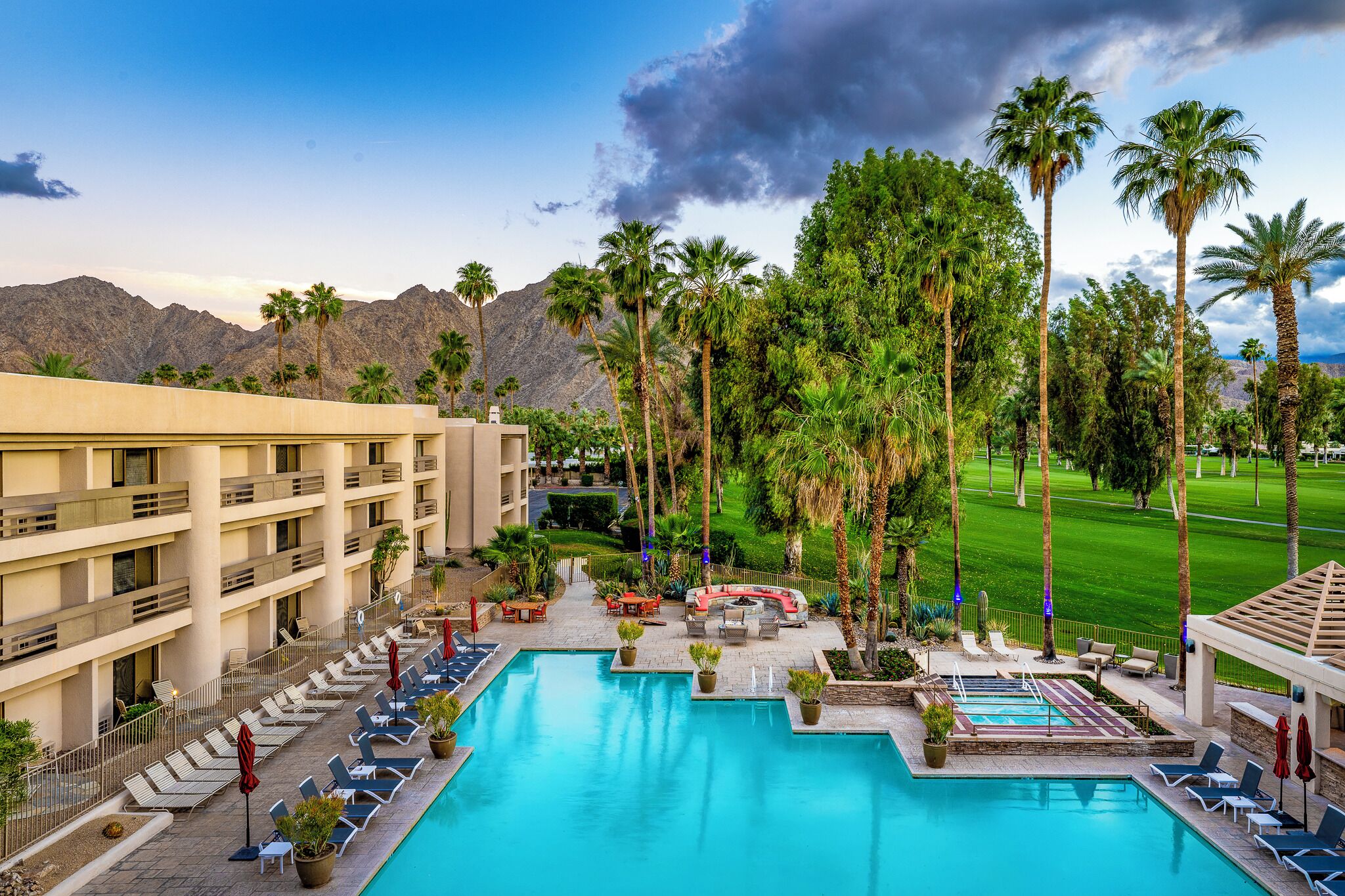 A hotel with a swimming pool, outdoor seating, and palm trees.