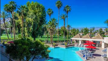 Zona de piscina con palmeras, sillas de descanso y vistas a un campo de golf.