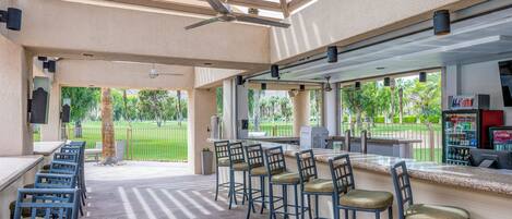 An outdoor bar area with a pool table, bar stools, and a grill.