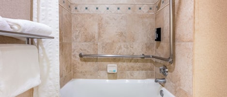 A bathroom with a bathtub, a handrail, and a towel rack.