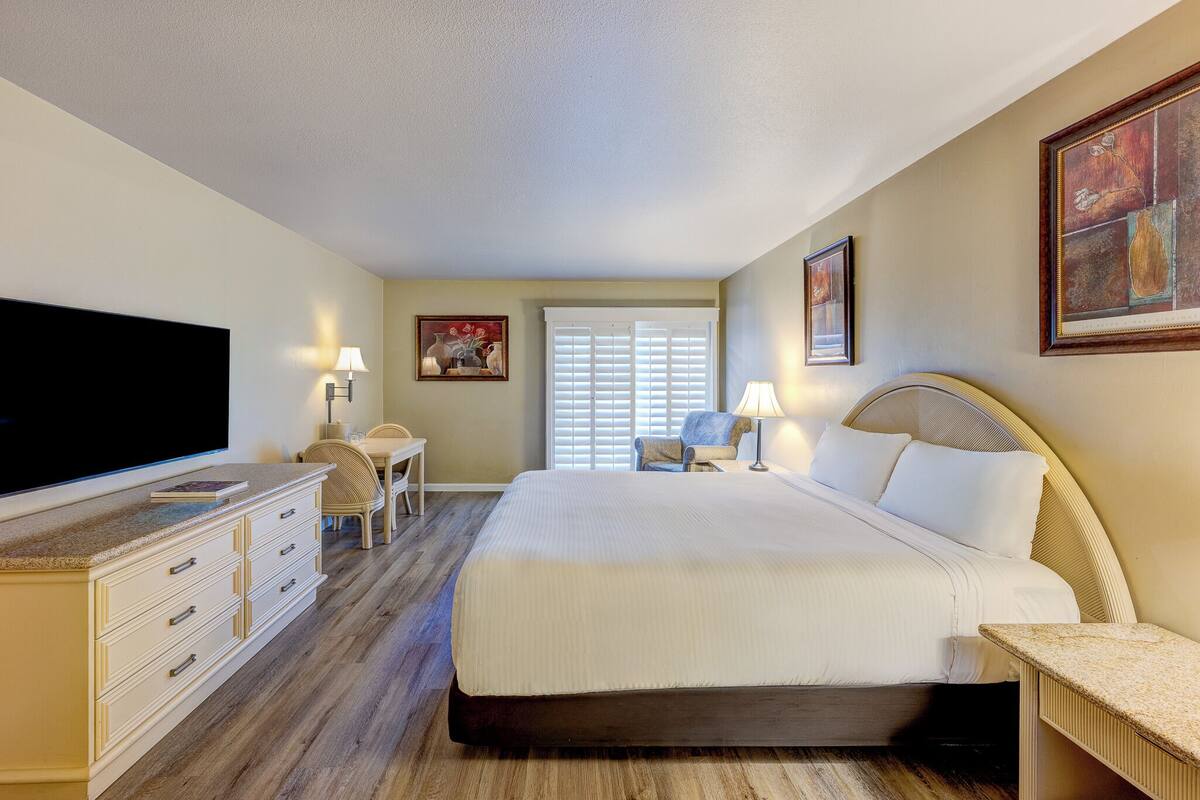 A hotel room with a large bed, a flat-screen TV, a desk, and a chair.