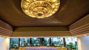 A ceiling with a circular light fixture, a view of palm trees, and a building in the background. - Indian Wells Resort Hotel (Indian Wells)