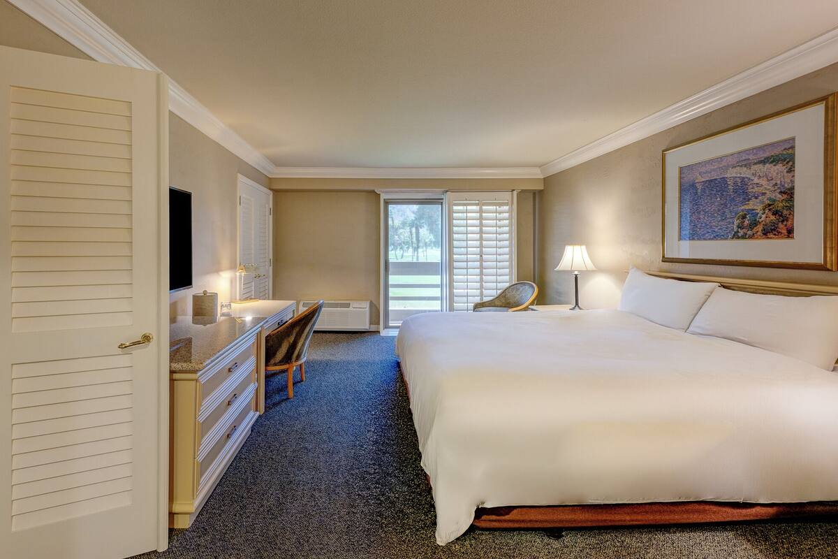 A hotel room with a bed, a desk, a chair, a television, and a painting on the wall.