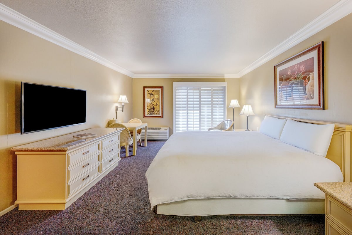 A hotel room with a bed, a TV, a desk, a chair, and a window with blinds.