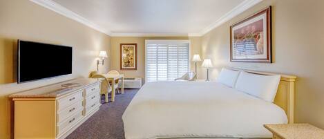 A hotel room with a bed, a TV, a desk, a chair, and a window with blinds.