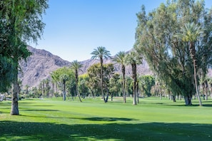 Ein Golfplatz mit Bäumen und Bergen im Hintergrund.