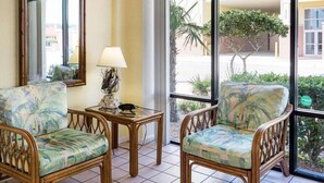 A room with two wicker chairs, a small table with a lamp, and a large window with a view of the outside. - Ocean 27 (Virginia Beach)