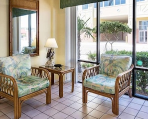 A room with two wicker chairs, a small table with a lamp, and a large window with a view of the outside. - Ocean 27 (Virginia Beach)