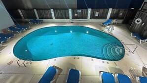 An indoor swimming pool with blue water, surrounded by blue lounge chairs and a wooden wall. - Ocean 27 (Virginia Beach)