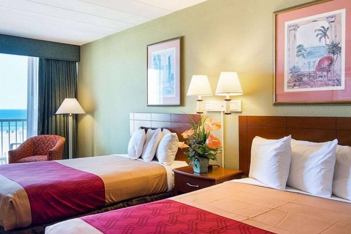 Habitación de hotel con dos camas, una silla, una mesita de noche con lámparas y obras de arte enmarcadas en las paredes.