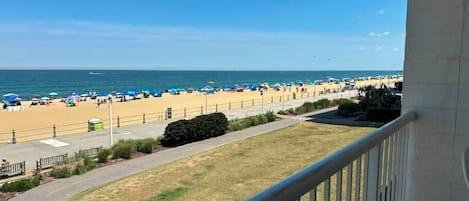 Blick auf einen Strand mit gepflastertem Weg, Sonnenschirmen und blauem Himmel.