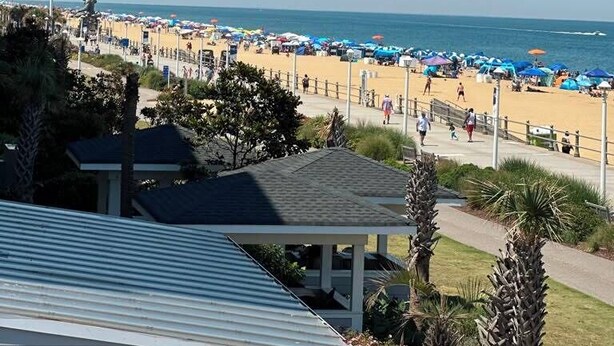 A beach with umbrellas and people, a statue, and a clear sky. - Ocean 27 (Virginia Beach)