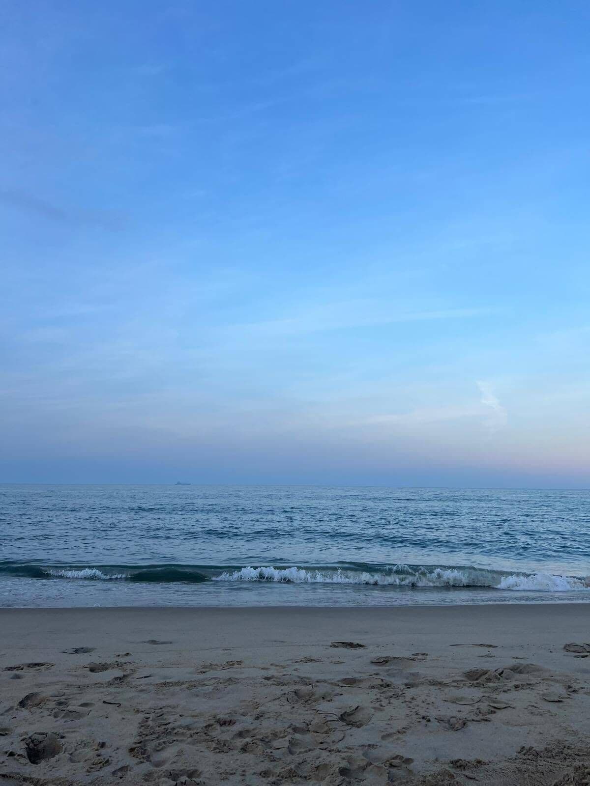 A beach with waves, a clear sky, and footprints in the sand.