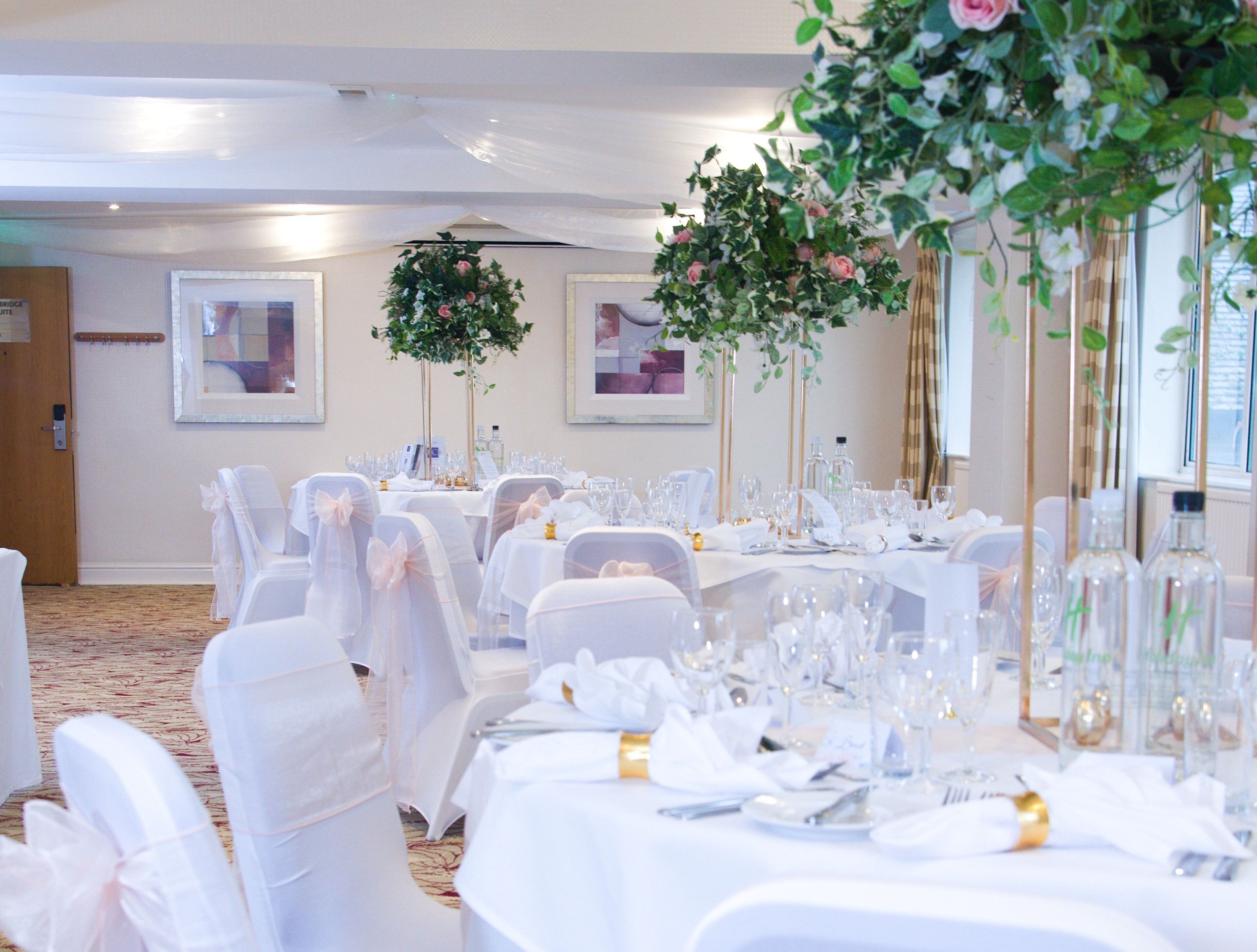 A banquet hall with round tables set for a formal event, white chairs, and floral centerpieces.