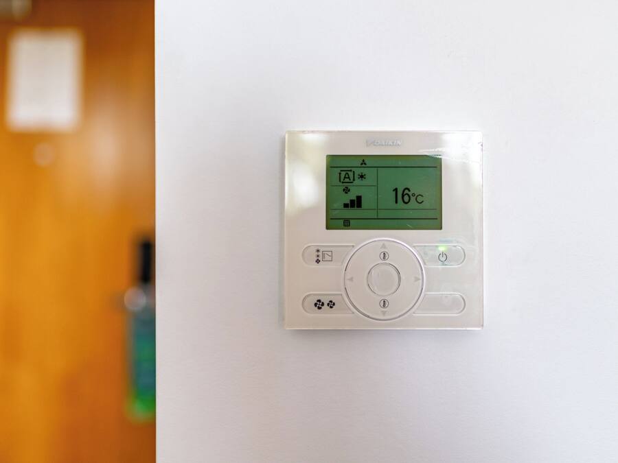 Un thermostat fixé au mur, doté d’un écran numérique indiquant une température de 16 degrés Celsius.