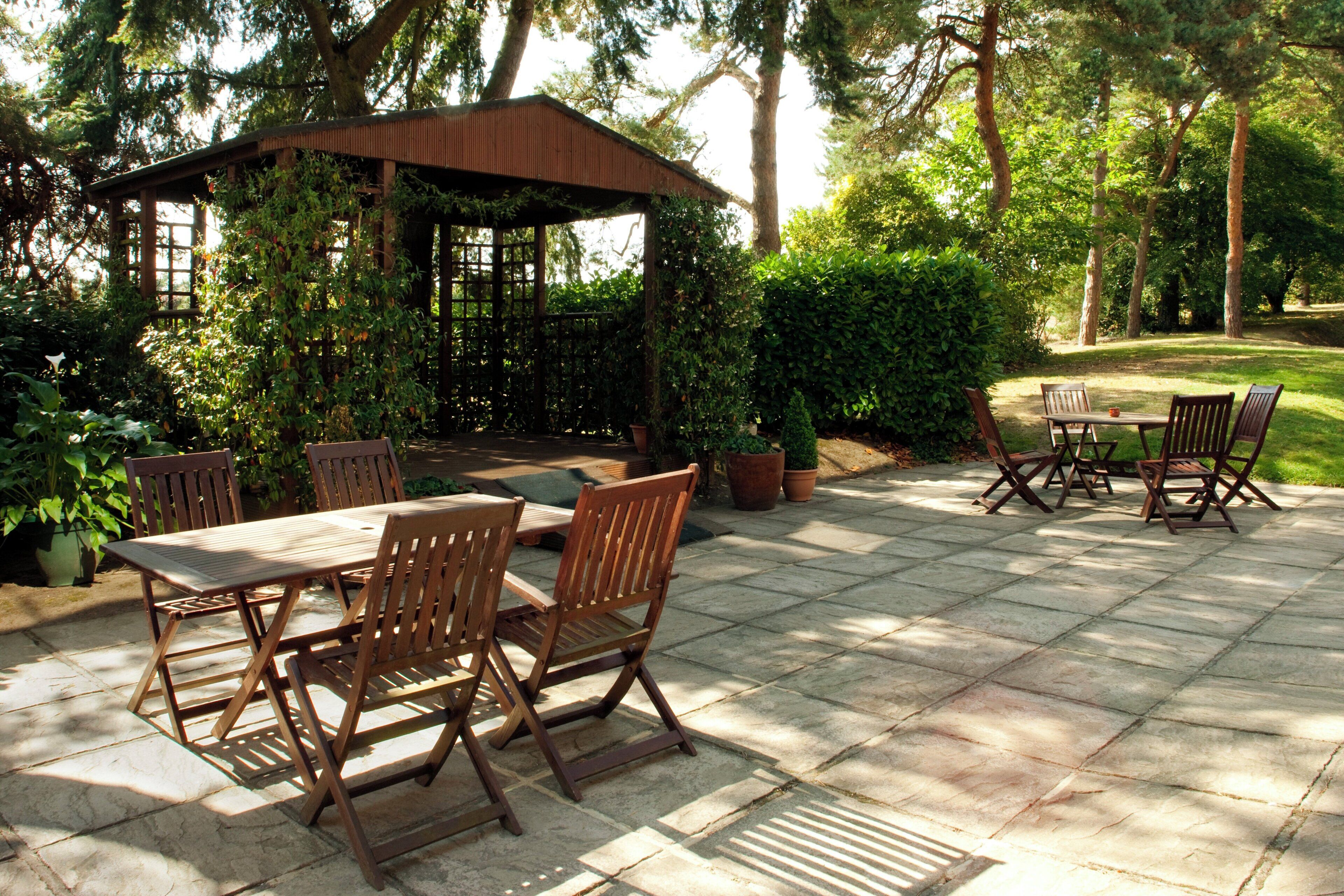 An outdoor patio with a wooden table and chairs, surrounded by potted plants and a pergola.