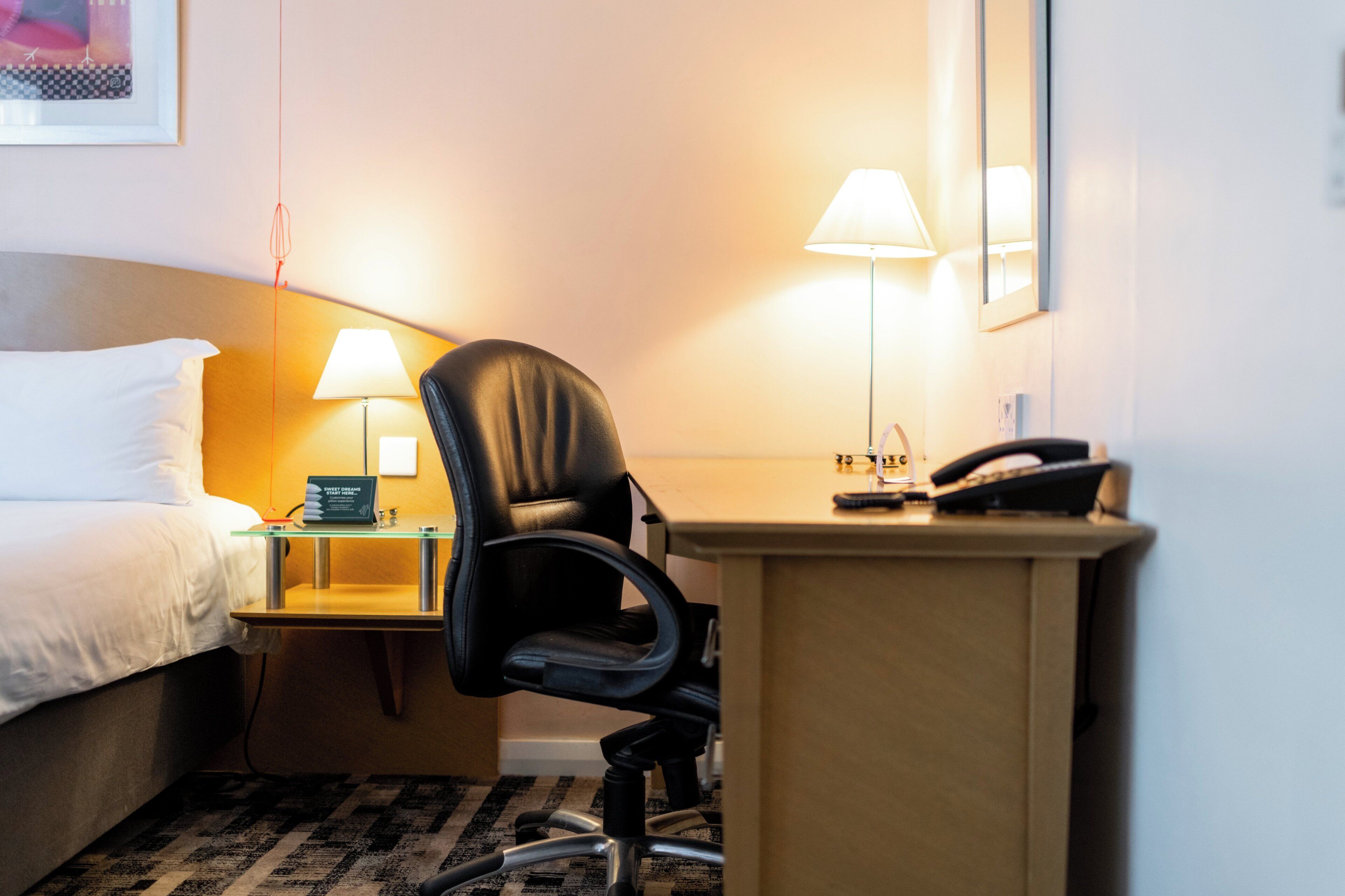 A hotel room with a bed, a desk with a lamp, a chair, and a telephone.