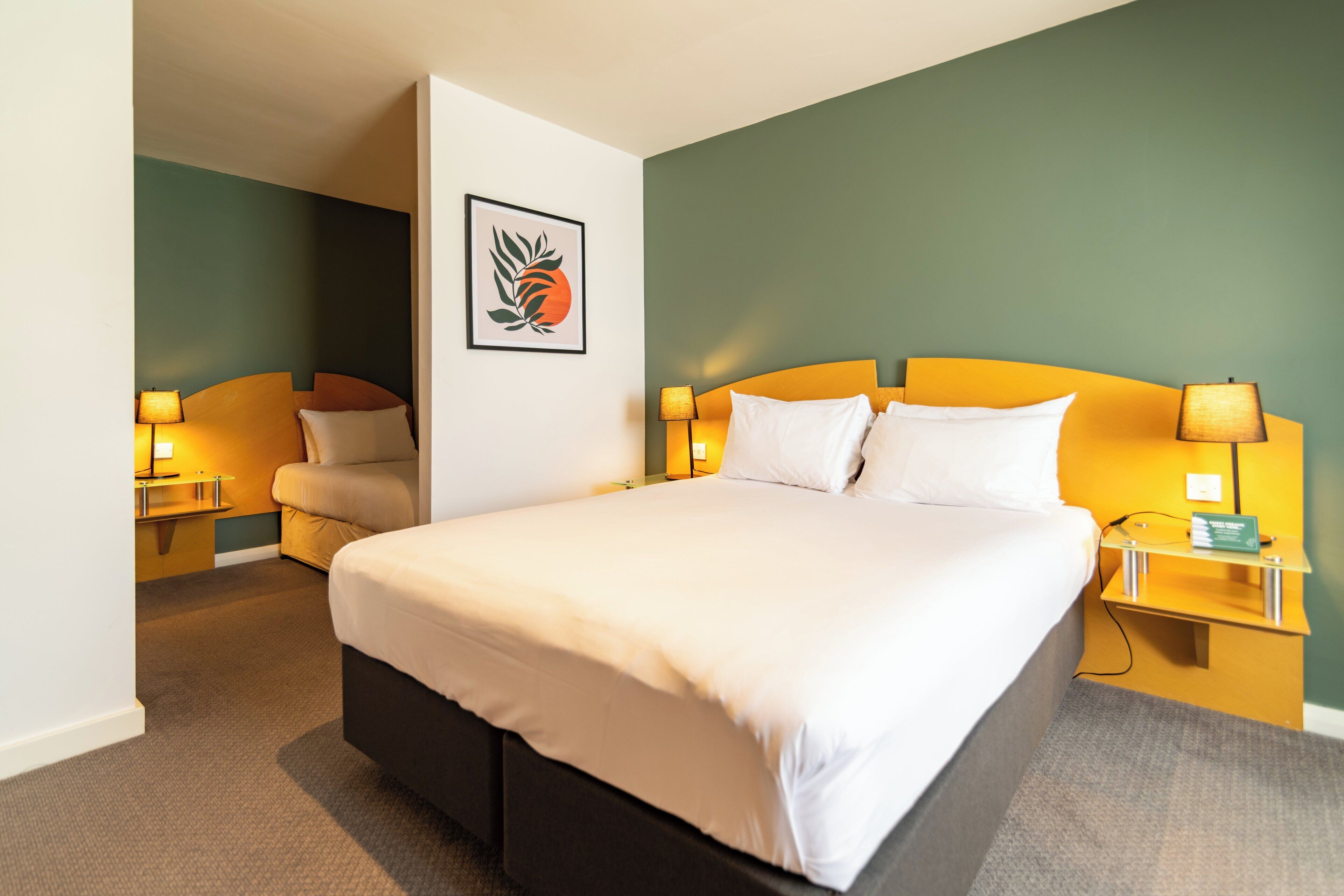 A hotel room with a large bed, two bedside tables, a chair, and a wall-mounted artwork.
