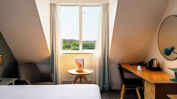 Ein Hotelzimmer mit Bett, Schreibtisch, Stuhl, einem kleinen Tisch und einem Fenster mit Vorhängen.