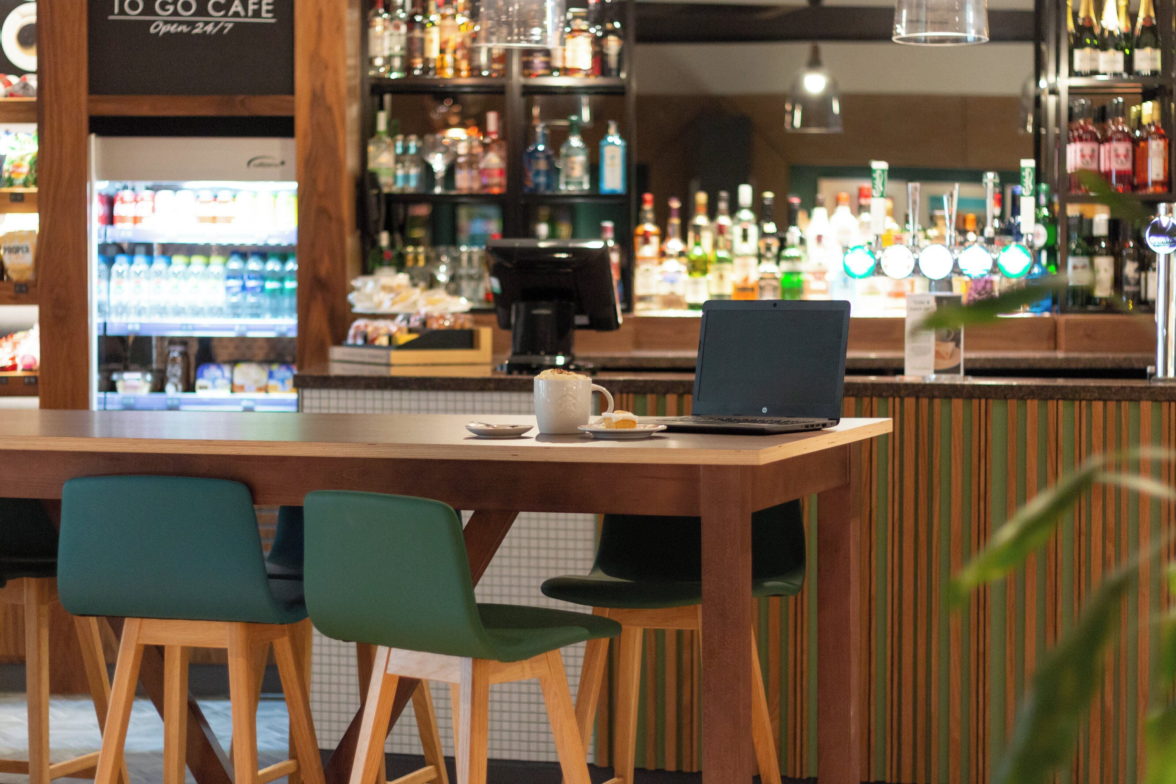 A bar area with a laptop on a table, two chairs, and shelves with bottles.