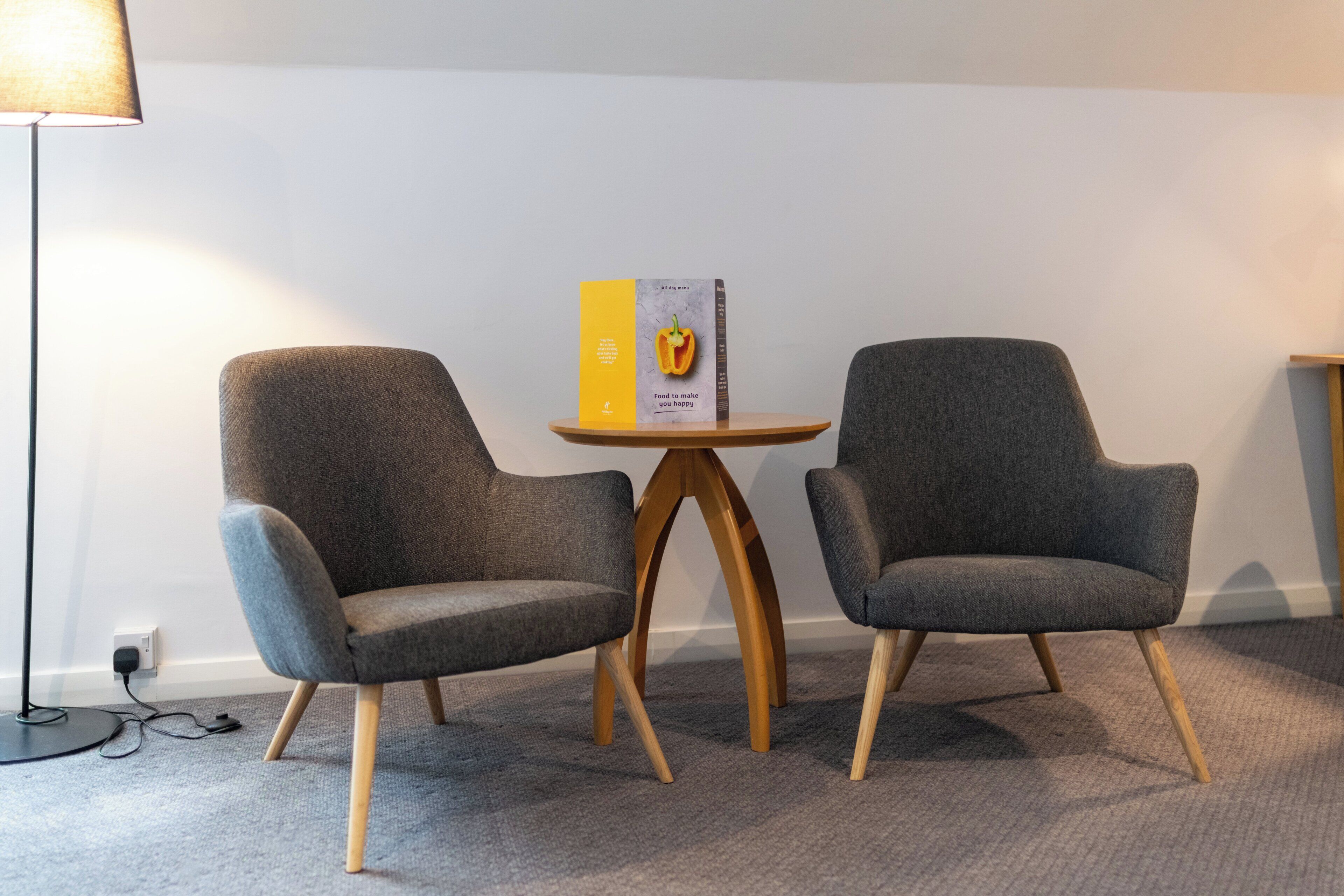 Twee grijze fauteuils met houten poten, een klein houten tafeltje en een lamp.