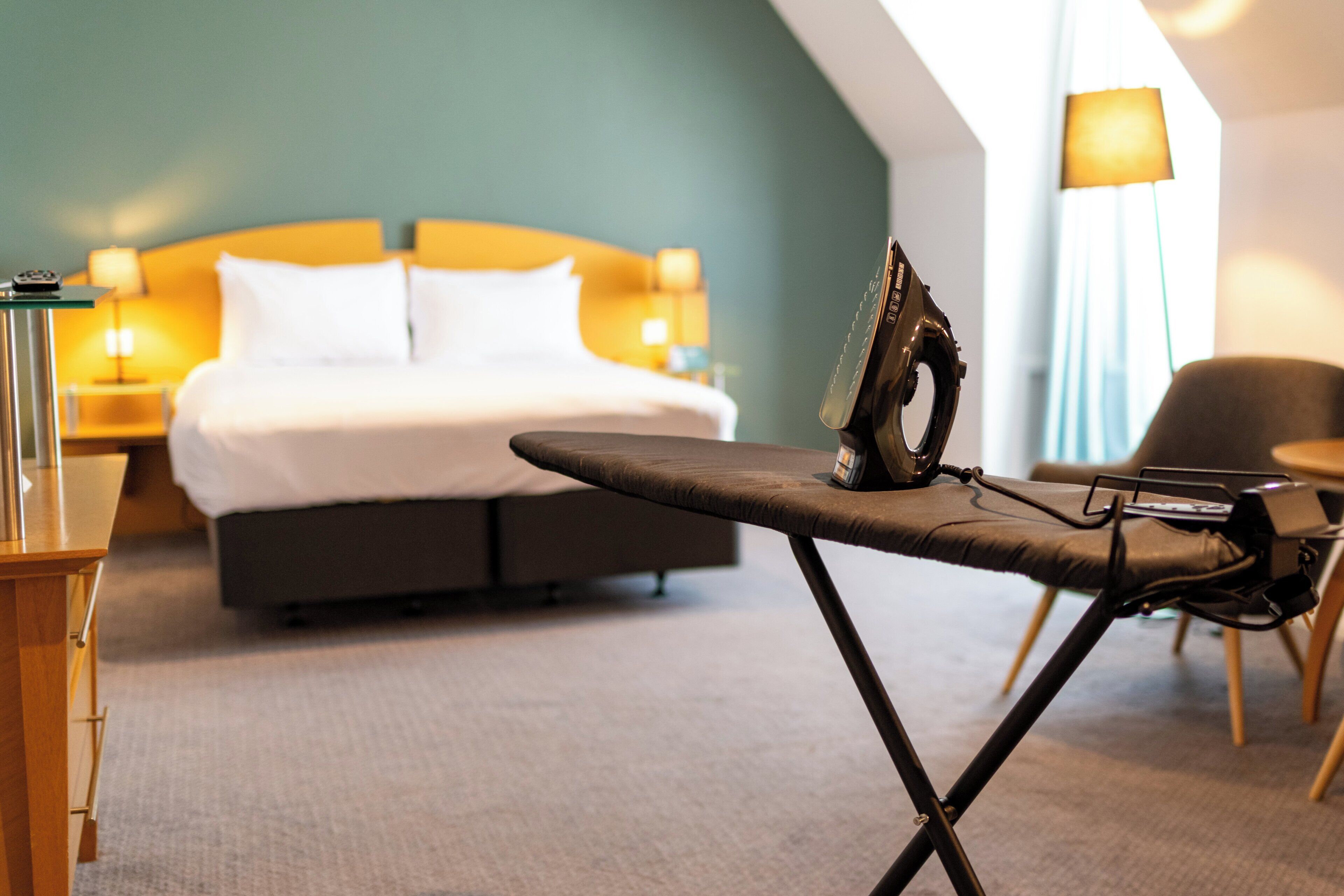 Une chambre d’hôtel équipée d’un lit, d’une planche à repasser, d’une chaise et d’une lampe.