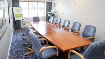 A conference room with a long table and multiple chairs, a clock on the wall, and a window with blinds.