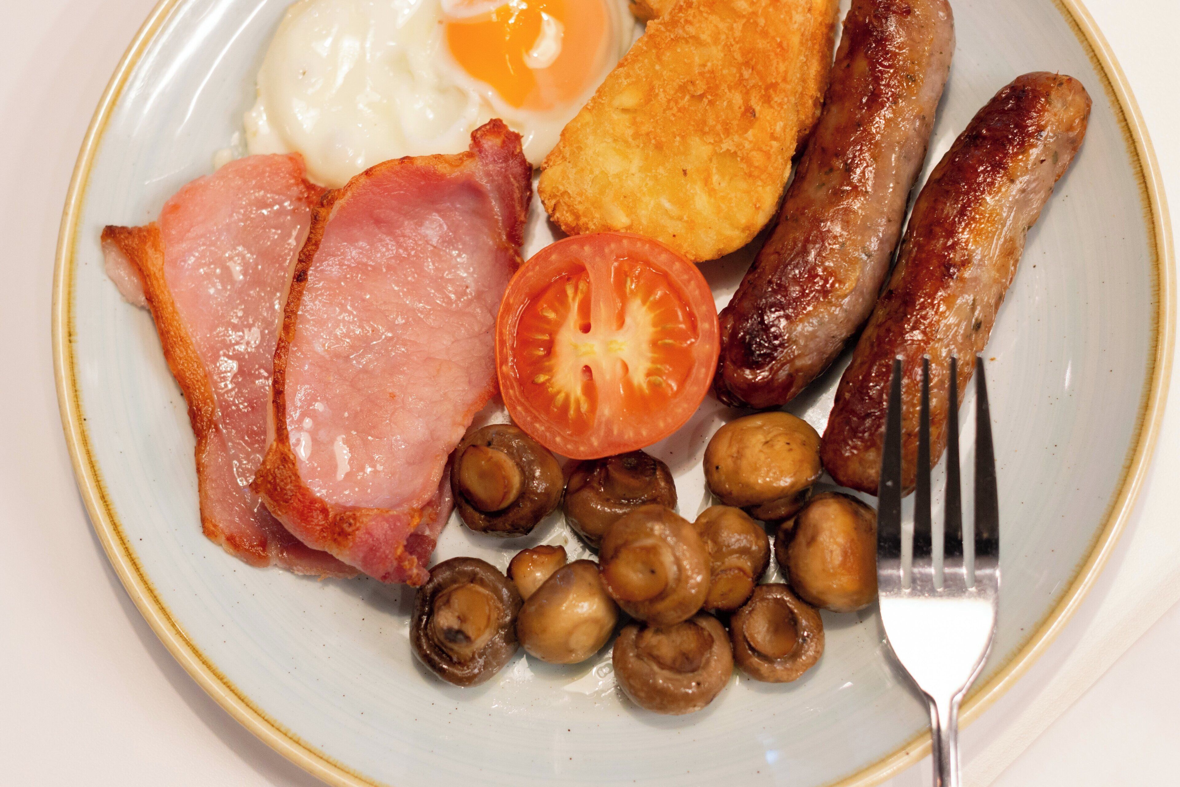 Une assiette de nourriture pour le petit-déjeuner comprenant des œufs, des saucisses, du bacon, des champignons et une tomate.