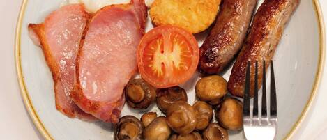 A plate of breakfast food including eggs, sausages, bacon, mushrooms, and a tomato.