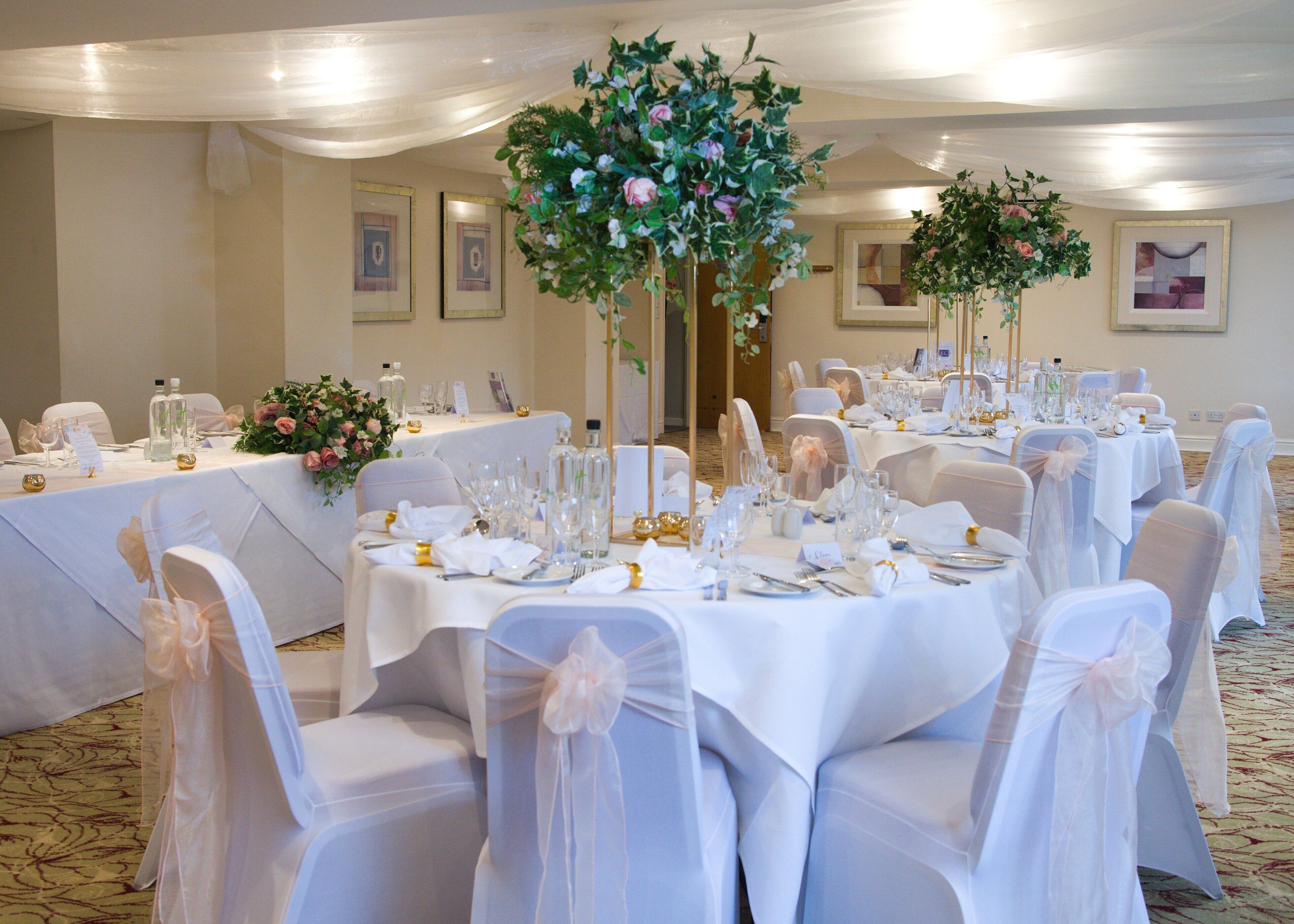 Een feestzaal met ronde tafels, klaar voor een formeel evenement, versierd met bloemdecoraties en witte tafelkleden.