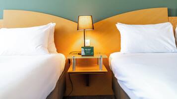 A hotel room with two single beds, a nightstand with a lamp, and a green box on the nightstand.