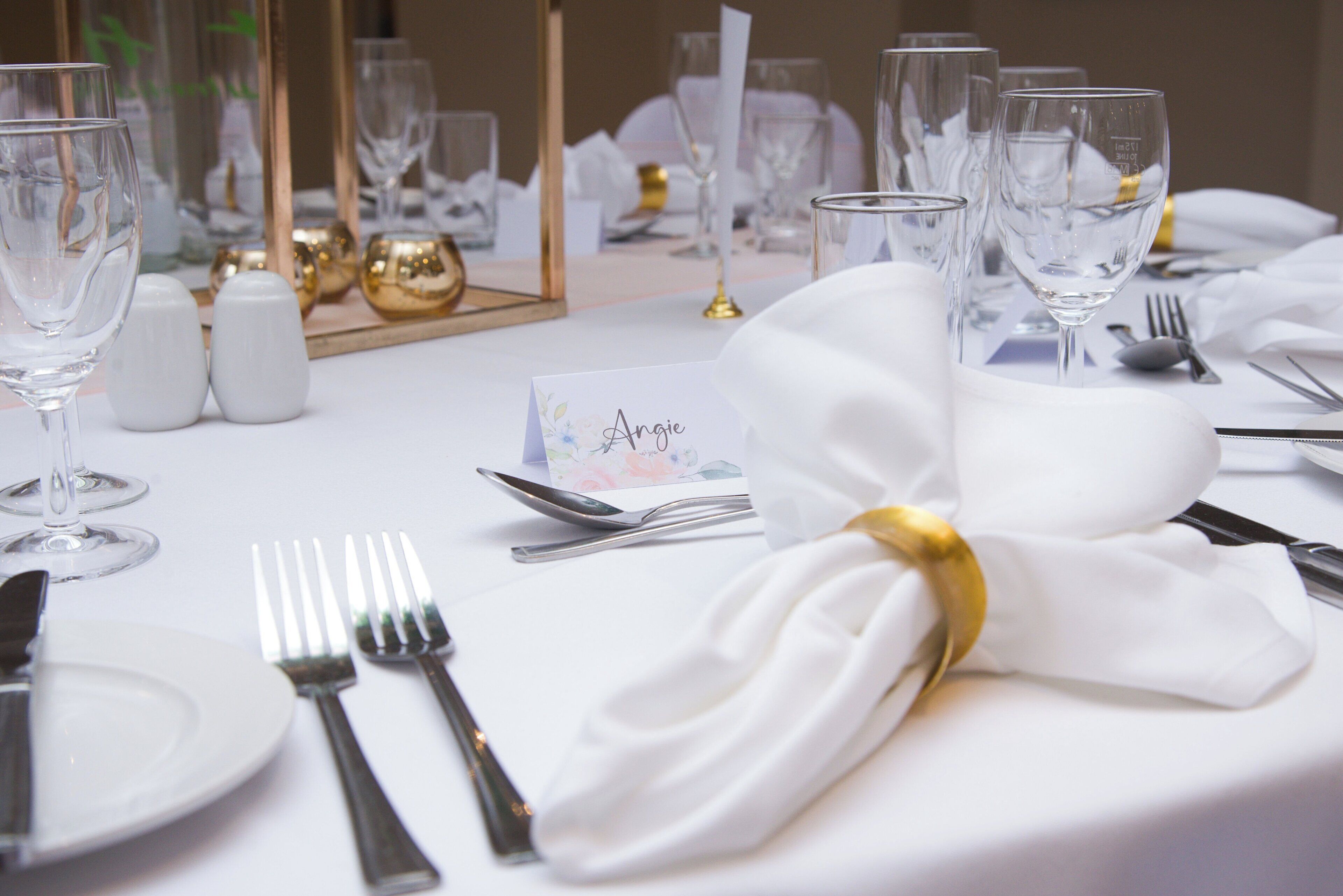 A table set for a formal event with white tablecloths, silverware, and clear wine glasses.