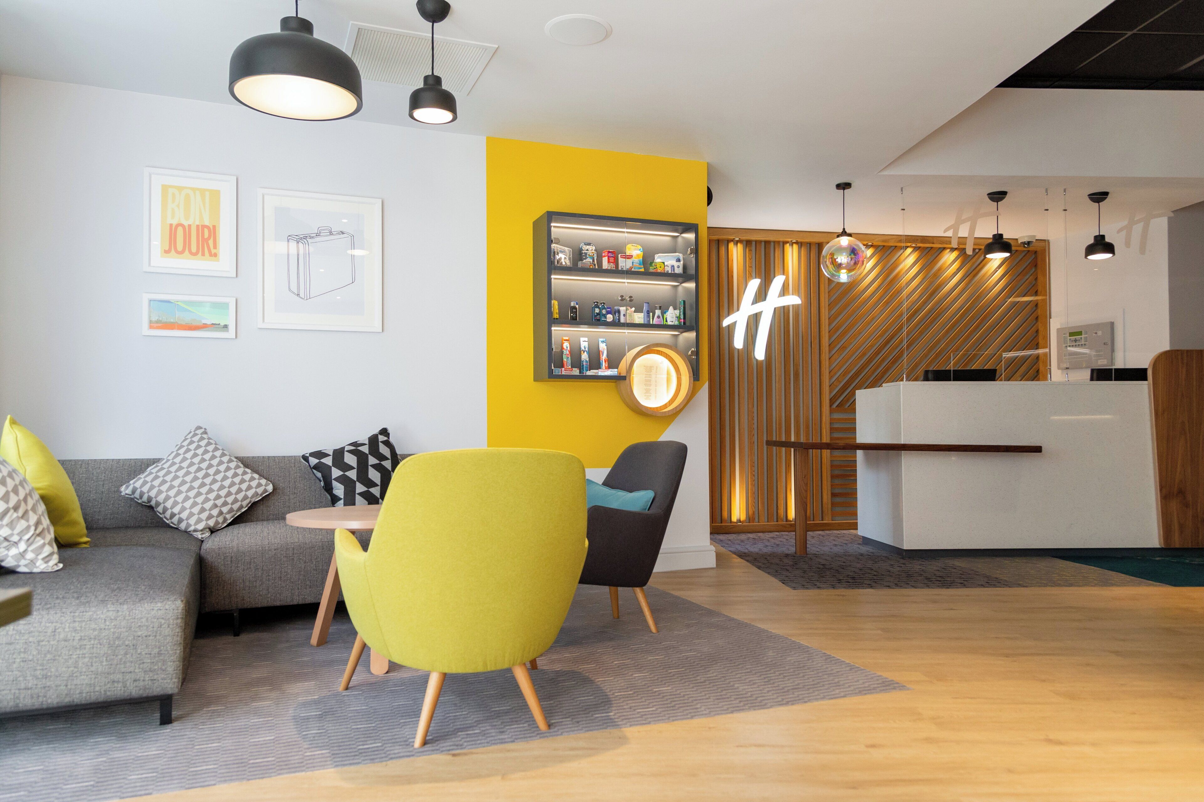 A modern hotel lobby with a grey sofa, yellow armchair, and a reception desk.