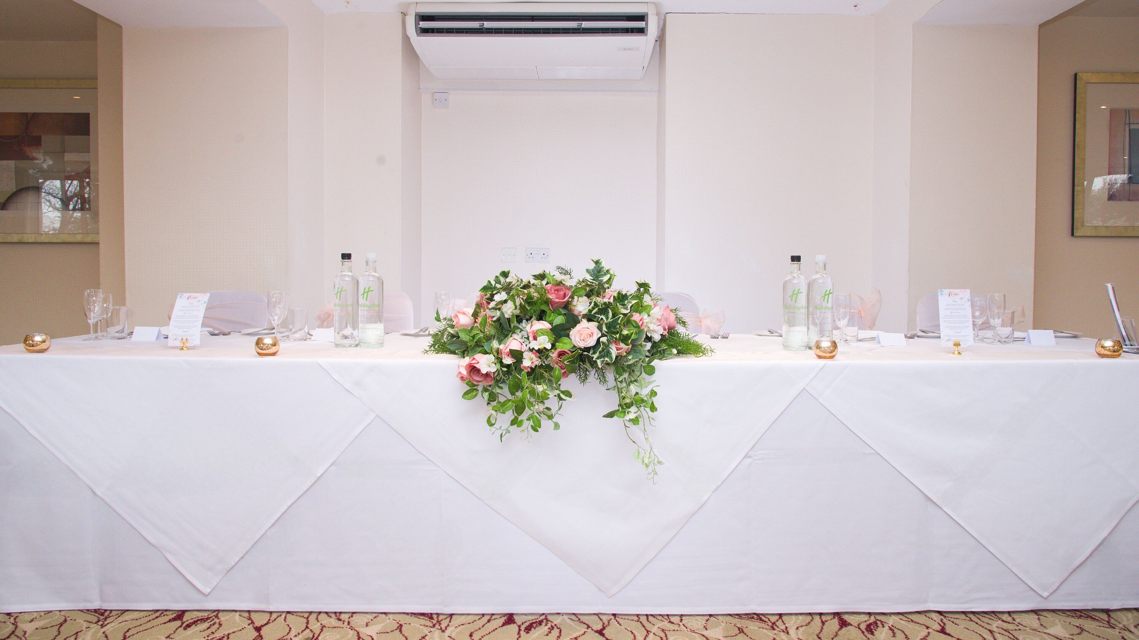 A banquet table set with a floral centerpiece, two bottles of water, and a menu sign.