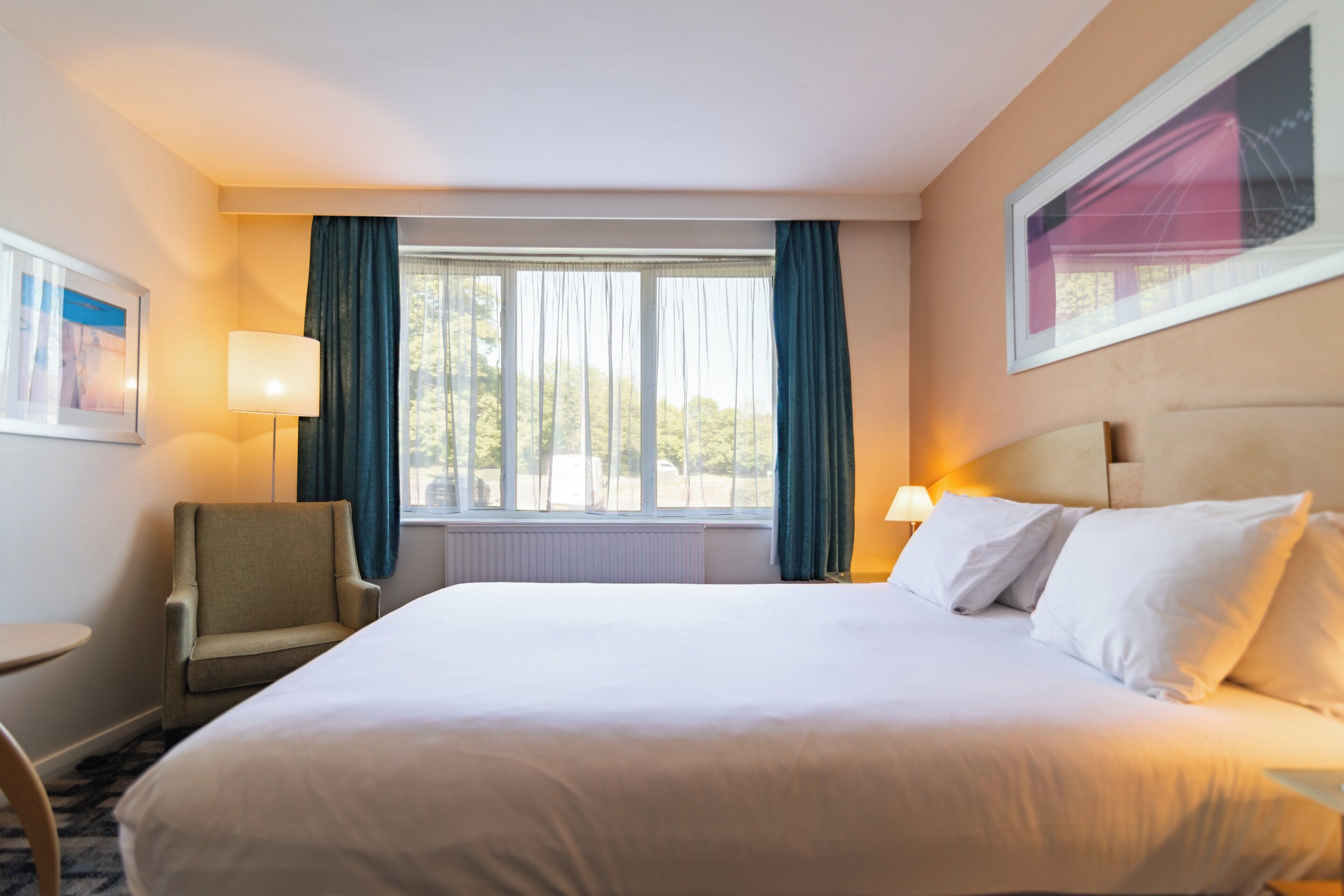 Habitación de hotel con una cama grande, una silla, un escritorio y una ventana con cortinas.