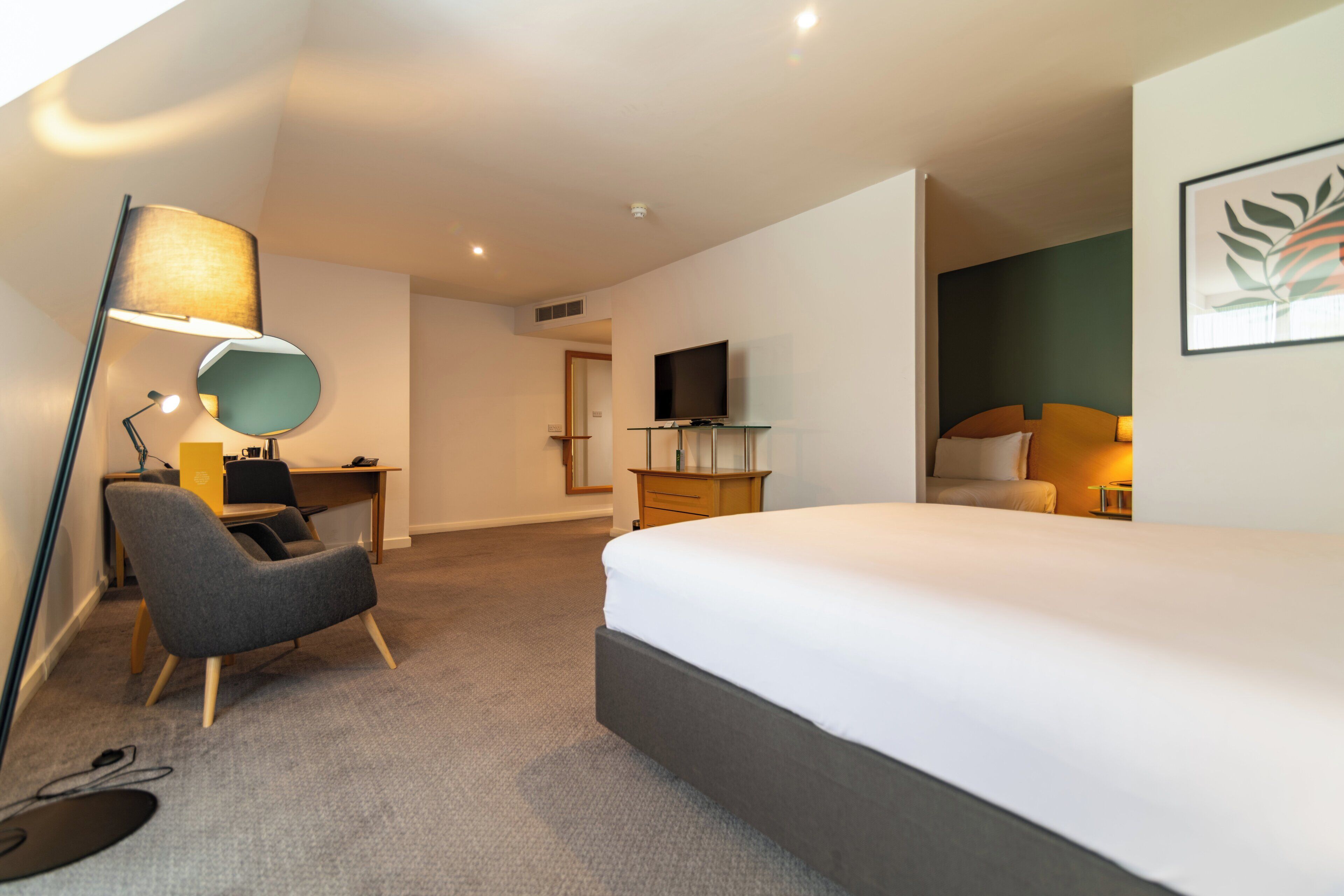 Een moderne hotelkamer met een groot bed, een bureau met stoel, een televisie en een lamp.