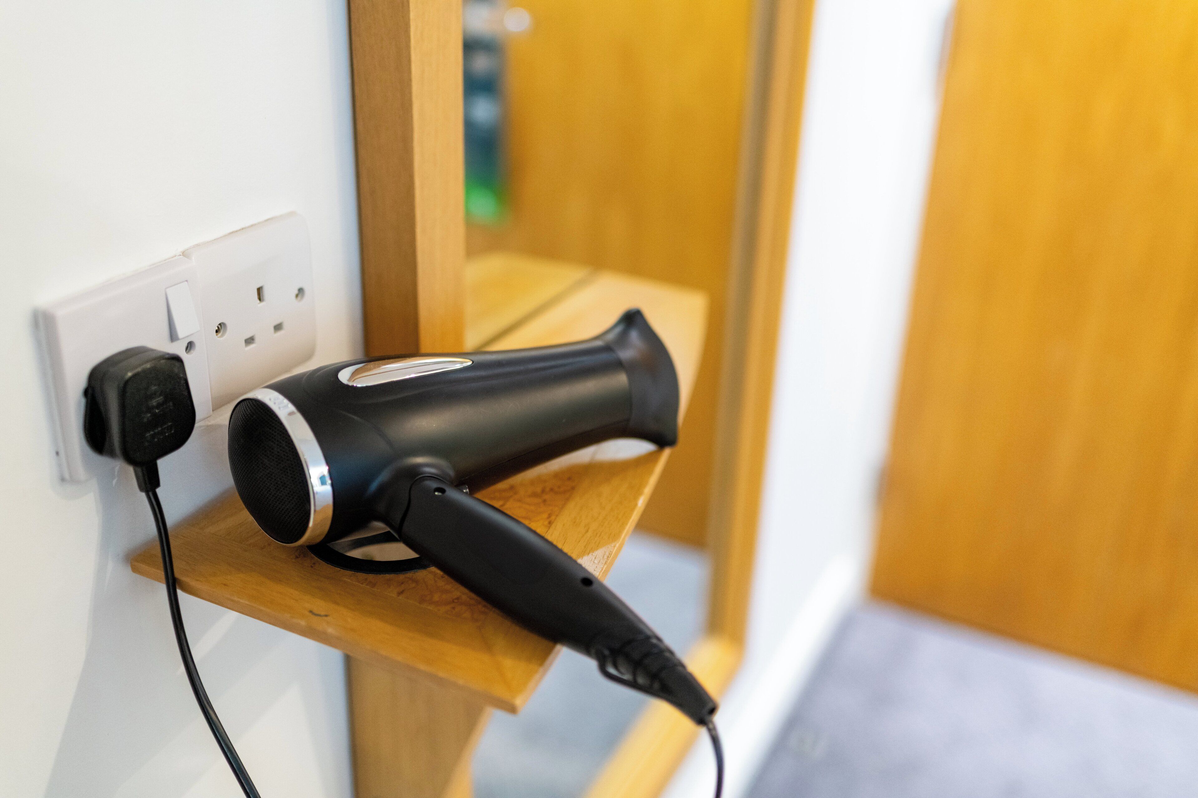 Un sèche-cheveux branché sur une prise électrique située sur une étagère en bois.