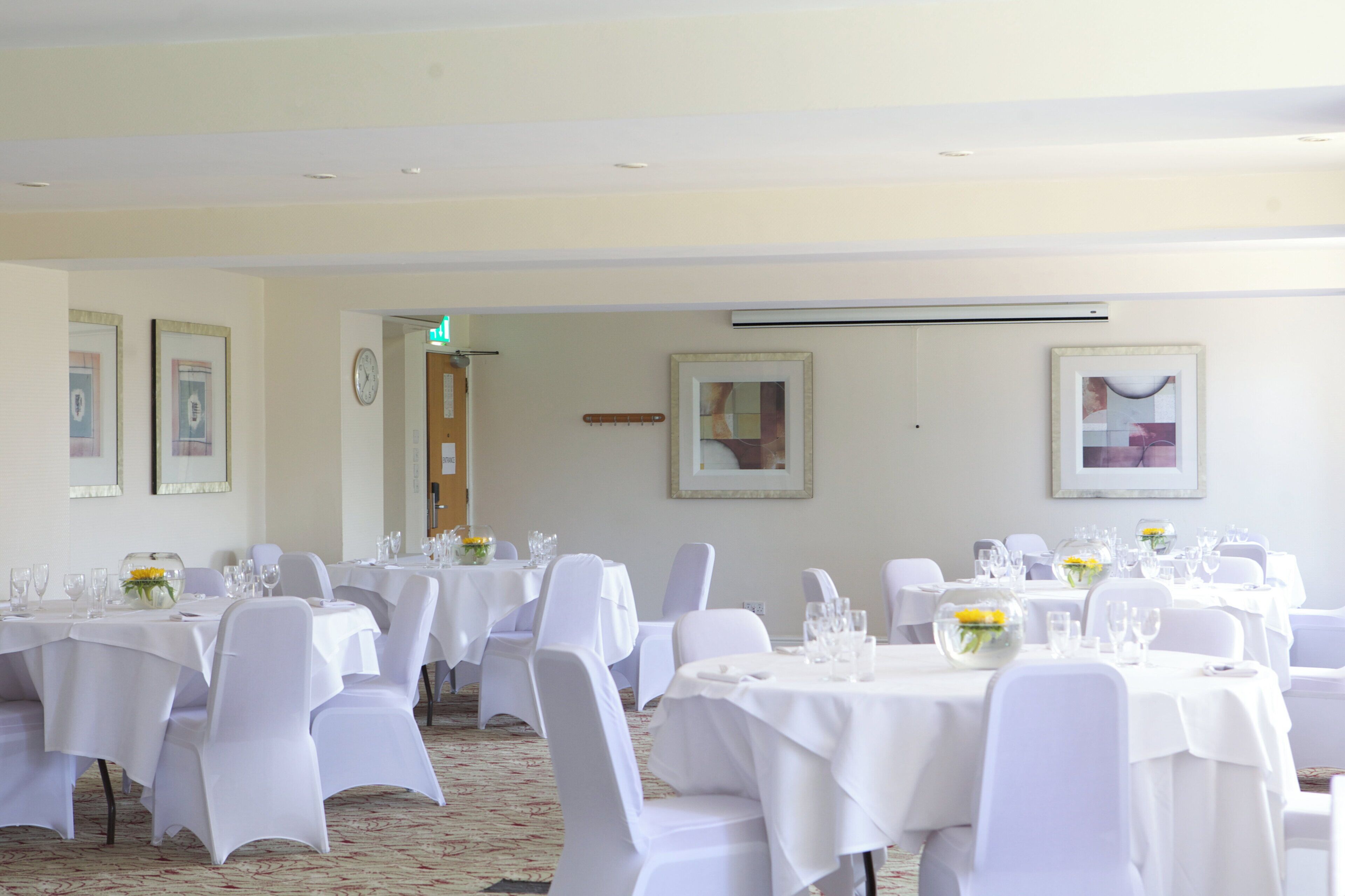A banquet hall with multiple round tables covered with white tablecloths, chairs, and glassware.