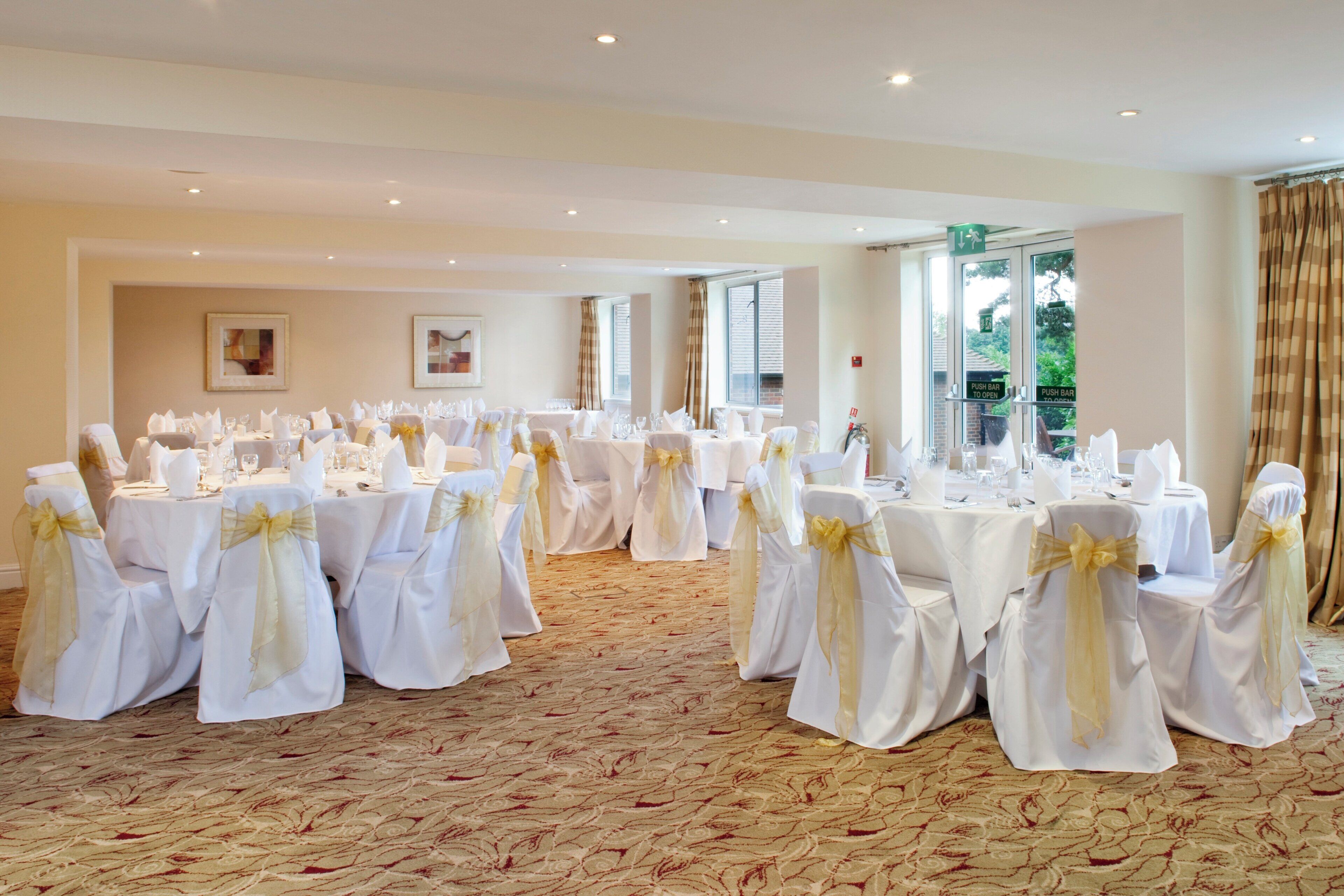 A banquet hall with round tables set for a formal event, featuring white tablecloths and chairs with gold sashes.